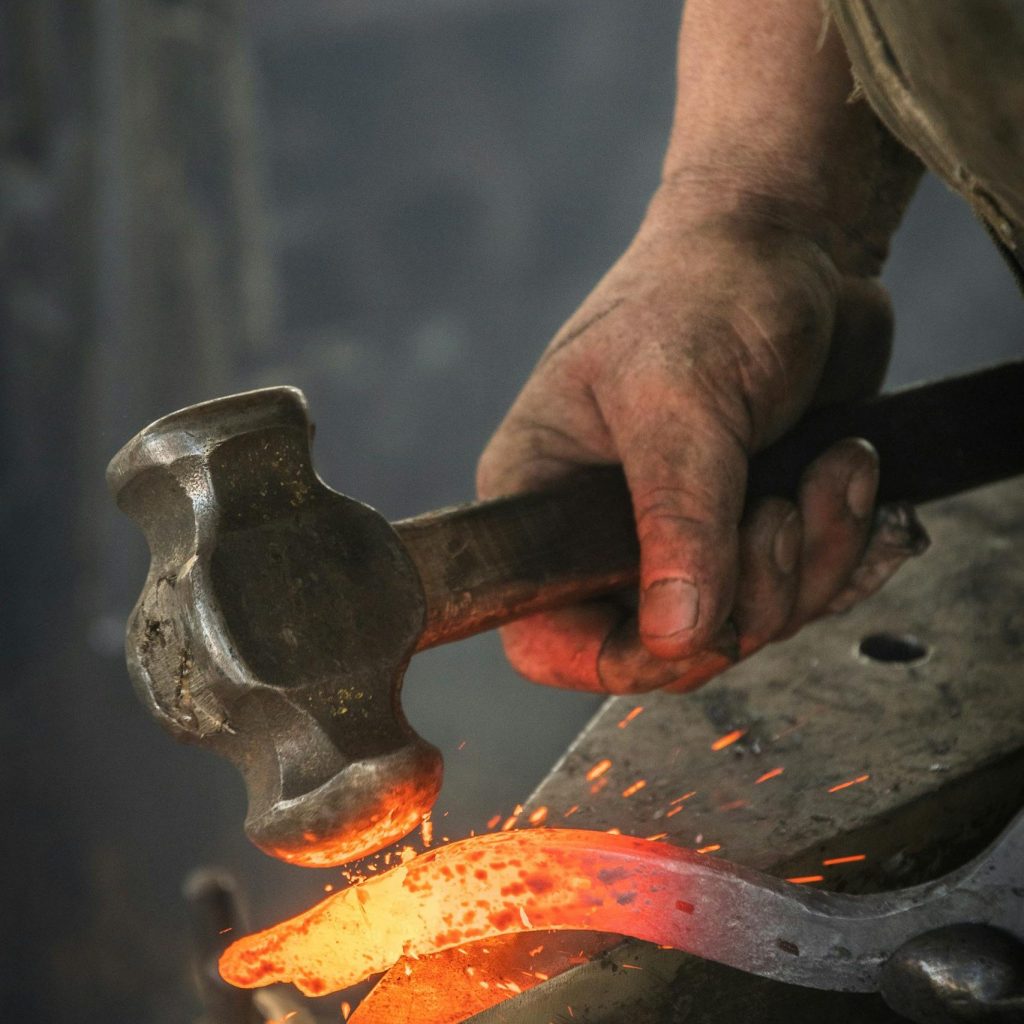Close-up of a blacksmith hammering a hot iron piece in a workshop.